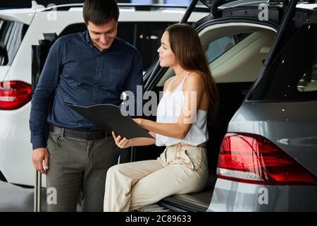 Nun wird ihr Traum wahr. Erfolgreicher Ehemann und seine liebevolle modische Frau lesen Auto Eigenschaften von neu gekauften Auto. Stockfoto