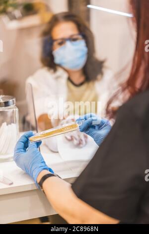 Vertikale Shallfokus-Aufnahme einer hispanischen Nagelkünstlerin Tragen einer Gesichtsmaske während der Arbeit Stockfoto