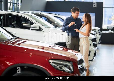 Kauf Ihr erstes Auto zusammen. Junge kaukasier positive Paar erfolgreicher Geschäftsmann und seine Frau umarmt in der Nähe von red glistering Auto Autohändler Stockfoto