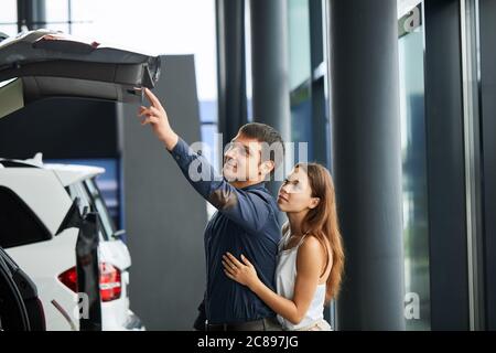 Nun wird ihr Traum wahr. Erfolgreicher Ehemann und seine liebevolle modische Frau untersuchen den Kofferraum des kürzlich gekauften Autos. Stockfoto