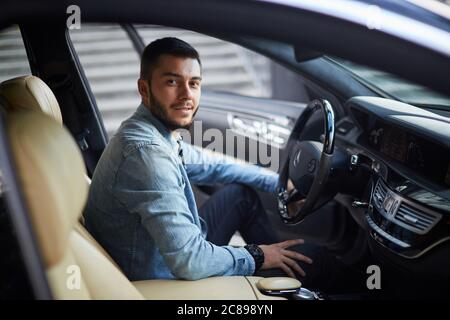 Super Mann sitzt mit geöffneter Tür im Fahrzeug. Schönheit und Maschinenkonzept. Seitenansicht Schuß Stockfoto