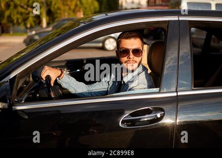 Attraktive junge Mann in trendigen Kleidung im Auto sitzen. Seitenansicht Foto.das Beste oder nichts Stockfoto