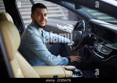 Super Mann sitzt mit geöffneter Tür im Fahrzeug. Schönheit und Maschinenkonzept. Seitenansicht Schuß Stockfoto