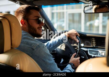Super Mann sitzt mit geöffneter Tür im Fahrzeug. Schönheit und Maschinenkonzept. Seitenansicht Schuß Stockfoto
