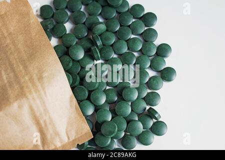 Grüne Pillen auf Holzlöffel isoliert auf weißem Hintergrund mit Reflexion. Spirulina, Chlorella und Weizengras. Gesundes Wohnkonzept. Stockfoto