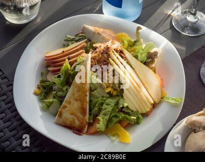 Nahaufnahme der weißen Platte mit frischem Gemüsesalat mit hausgemachtem Ziegenkäse, Salat, Birne und karamellisierten Nüssen auf Meeresfrüchte-Restauranttisch Stockfoto