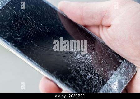 Ein junger Mann hält ein Telefon mit einem sehr geknackten Touchscreen Stockfoto