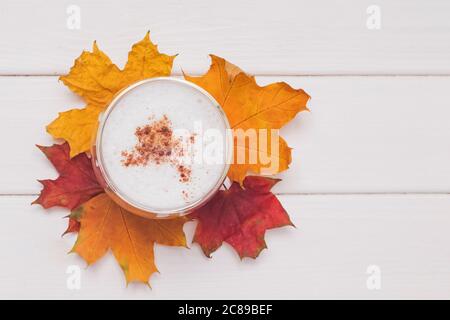 Kaffee Latte mit Schaum und Zimt und gelben und roten Blättern auf weißem Tisch Stockfoto