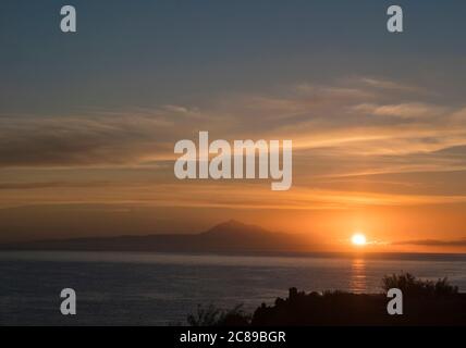 Wunderschöner orangefarbener Sonnenaufgang über dem ruhigen Meer und dem Pico del Teide auf Teneriffa von La Palma aus gesehen Stockfoto