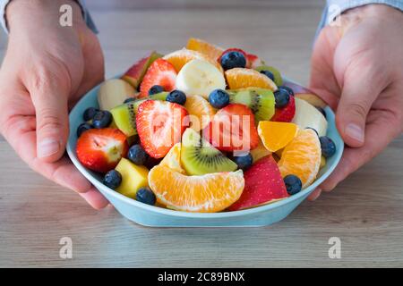 Frischer Obstsalat, der Mann hält einen Teller voll geschnittener Früchte über den Tisch Stockfoto