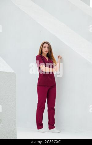 Medizinstudenten in burgunderroten OP-Anzügen stehen vor der Krankenpflegeschule. Junge Mädchen Gynäkologen Arzt. Stockfoto