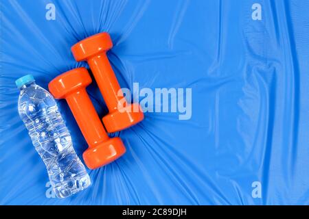 Orange Kurzhanteln und Wasser auf blauer Matte mit Kopierraum Stockfoto