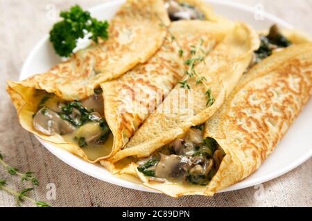 Herzhafte hausgemachte Pilzbecherei, Spinat und Käsecrepes auf einem weißen Teller, Seitenansicht. Nahaufnahme. Stockfoto