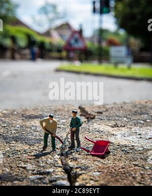 Miniaturmenschen, zwei Arbeiterfiguren, die einen Riss in der Straße in Lennoxtown, Schottland reparieren Stockfoto