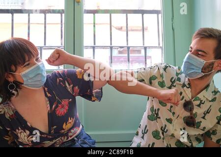 Junge kaukasische Paar trägt Gesichtsmasken und Gruß mit Ellenbogen Beule. Coronavirus neues Normalitätskonzept. Stockfoto