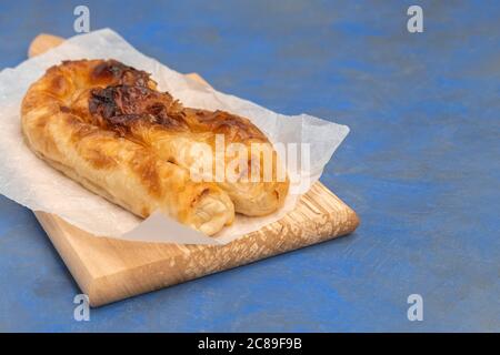 Traditionelles bulgarisches Käsegebäck Banitsa auf Holzbrett auf dunkelblauem Grund, Kopierraum Stockfoto