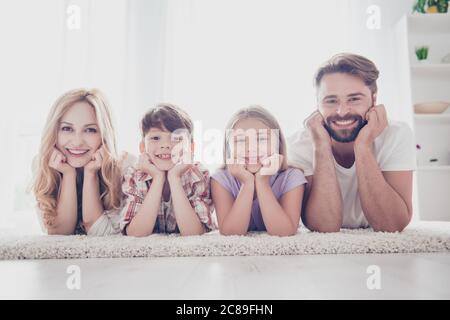 Happy Family Konzept. Vier Verwandte liegen auf dem Teppich auf dem Boden, halten Köpfe mit Armen, lächelnd, zu Hause Stockfoto