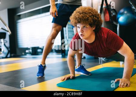 Fette junge Männer mit Trainer-Training im Fitness-Studio. Stockfoto