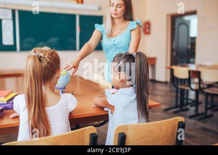 Geografie-Lehrerin zeigt zwei Schülerinnen auf einer Welt, Einzelunterricht, Wahlfach Stockfoto