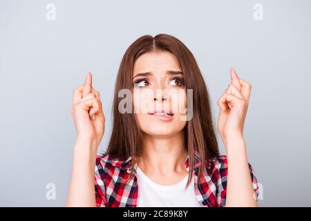 Junge nette Brünette Dame hält die Daumen gedrückt und schaut nach oben, in der Hoffnung auf Glück, bevor Sie zu Vorstellungsgespräch oder Prüfung auf reinem Hintergrund, in ch Stockfoto