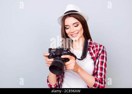 Junge attraktive Brünette Fotograf lächelt auf dem blauen Hintergrund. Sie ist aufgeregt und hält Kamera, trägt Sommerhut, die Fotos zu sehen Stockfoto