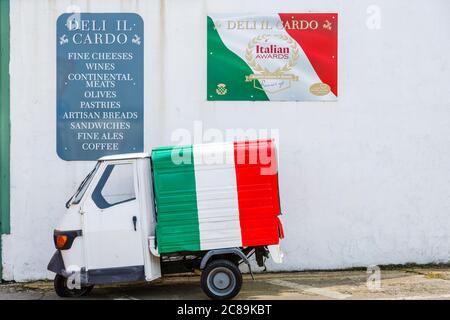 Largs, North Ayrshire, Schottland, Großbritannien. Deli Il Cardo Café Schilder und ein Piaggio Ape 50 Lieferwagen mit den Farben der italienischen Nationalflagge gemalt Stockfoto