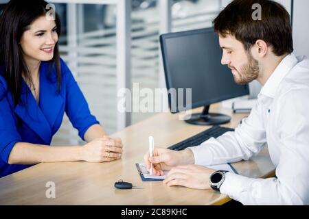 Der Verkäufer schreibt die Bemerkungen der weiblichen Kunden in einem Notebook auf, das im Besprechungsraum sitzt Stockfoto