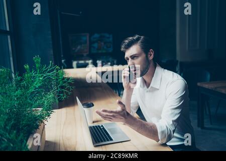 Selbstbewusster, hübscher junger Mann führt ein Geschäftsgespräch, am Arbeitsplatz in einem modernen Coworking, gestikulierend, gut gekleidet Stockfoto