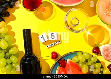 Trauben, eine Flasche Wein und verschiedene Früchte auf gelbem Hintergrund. Deutscher Text August 15, traditioneller italienischer Erntetag und Feiertag in Italien. Das Symbol für Spaß und Feier. Hartes Licht. Stockfoto