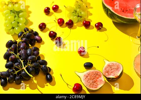 Trauben, eine Flasche Wein und verschiedene Früchte auf gelbem Hintergrund. Das Konzept der Ernte, Spaß und Feier in Italien und Spanien. Fotos bei hartem Licht. Hochwertige Fotos Stockfoto