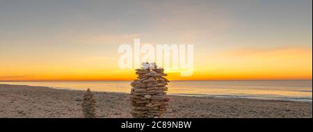 Kieselsteinpfeilern am Strand bei Sonnenuntergang, Zen-Atmosphäre. Stockfoto