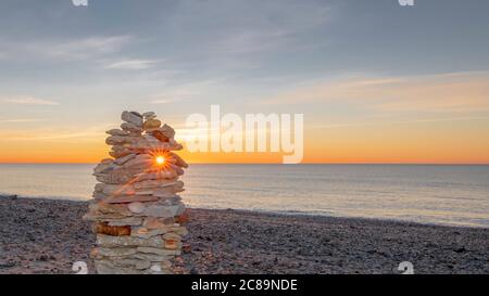 Kieselsteinpfeilern am Strand bei Sonnenuntergang, Zen-Atmosphäre. Stockfoto