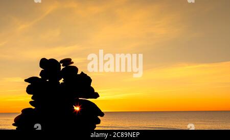 Kieselsteinpfeilern am Strand bei Sonnenuntergang, Zen-Atmosphäre. Stockfoto