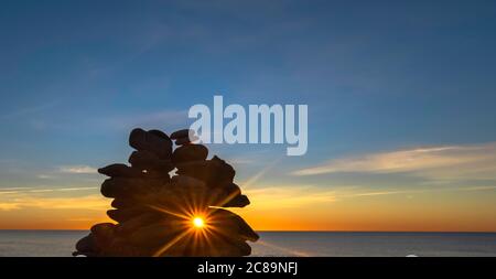 Kieselsteinpfeilern am Strand bei Sonnenuntergang, Zen-Atmosphäre. Stockfoto