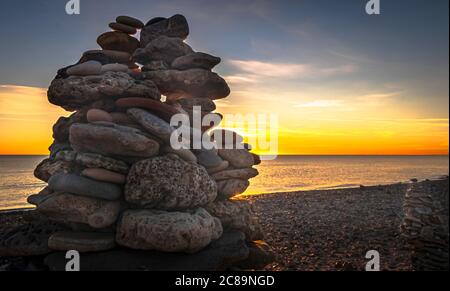 Kieselsteinpfeilern am Strand bei Sonnenuntergang, Zen-Atmosphäre. Stockfoto