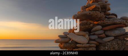 Kieselsteinpfeilern am Strand bei Sonnenuntergang, Zen-Atmosphäre. Stockfoto