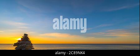 Kieselsteinpfeilern am Strand bei Sonnenuntergang, Zen-Atmosphäre. Stockfoto