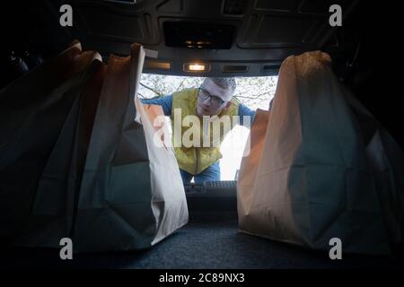 Männlicher Ladendalismus Konzept. Schöner Kerl, der Papiertaschen in den Kofferraum des Autos legt Stockfoto