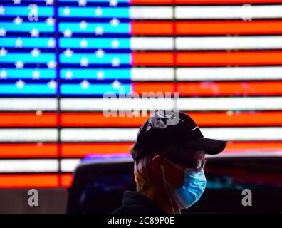 New York, New York-2020. Mai: Ein Mann mit Schutzmaske geht auf dem New Yorker Times Square an einer digitalen amerikanischen Flagge vorbei. Stockfoto