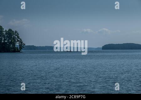 Eine Silhouette von Menschen, die auf einem Boot auf dem See mit einem trüben Hintergrund an einem heißen sonnigen Tag im Sommer fischen Stockfoto