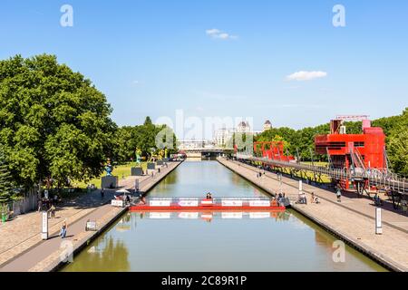 Der Canal de l'Ourcq teilt den Parc de la Villette in Paris, Frankreich, der von einer beweglichen, schwimmenden Fußgängerbrücke durchzogen und von Statuen und Torheiten begrenzt wird. Stockfoto