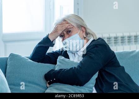 Einsame depressive ältere Witwe Frau mit Schutzmaske weinend auf Couch isoliert zu Hause, traurig und besorgt vermissten Mann und Familie in COVID-19 Deat Stockfoto
