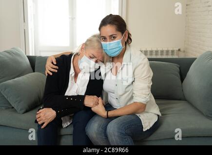 Depressive ältere Mutter und Tochter tragen medizinische Maske weinen und umarmen einander trauernden Verlust von Angehörigen kämpfen das Coronavirus. Menschen Stockfoto