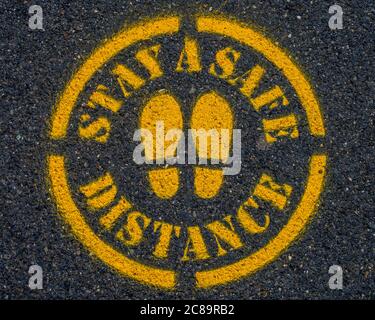 Covid-19 Bleiben Sie ein sicheres Distanzschild auf dem Bürgersteig oder der Straße. Stockfoto