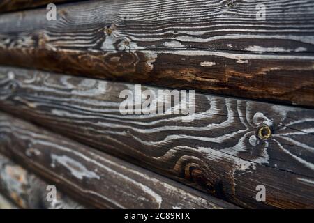 Rustikale Textur an der Wand im Freien, Seitenansicht, dunkler Hintergrund. Selektiver Fokus von braunen alten Volumen rauen Holzplanken, erstaunliche natürliche Muster für Design und Dekoration. Konzept der natürlichen Einrichtung. Stockfoto