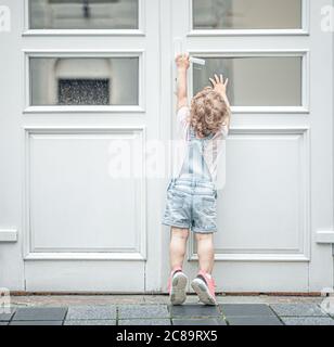 Kind versucht, die Tür zu öffnen. Das Kind greift auf der Straße nach dem Türknopf. Stockfoto