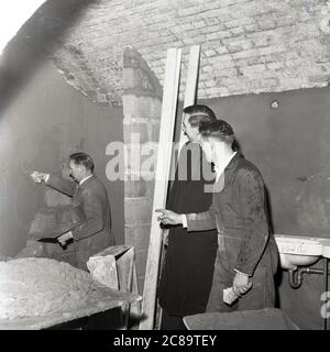 1960er Jahre, historische, Reparaturen an der Krypta, St. Pauls, Deptford, Southeast London, ein Arbeiter verputzt einen der Keller Ziegel Wal's. Priester mit Arbeitern, die Reparaturen an der Krypta durchführen. In den 1980er Jahren war das Untergeschoss der Ort für Raves und Gigs, darunter die Band The Stone Roses Stockfoto