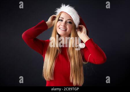 Innenaufnahme von staunenden blonden langhaarigen weiblichen Weihnachtsmann in Hut und roten Kleidern, Posen gegen schwarze Wand mit leeren Kopie Raum. Stockfoto