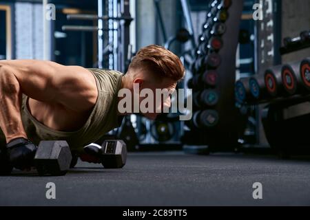 Side Nahaufnahme von muskulösen Mann Training auf dem Boden mit Humbbels im Sportverein. Ernte der jungen Sportler Gebäude Muskeln, tun Liegestütze in leeren Turnhalle. Konzept des Sports, Bodybuilding. Stockfoto