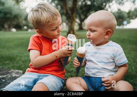 Baby und Kleinkind teilen sich etwas Eis und schauen sich jedes an Andere Stockfoto